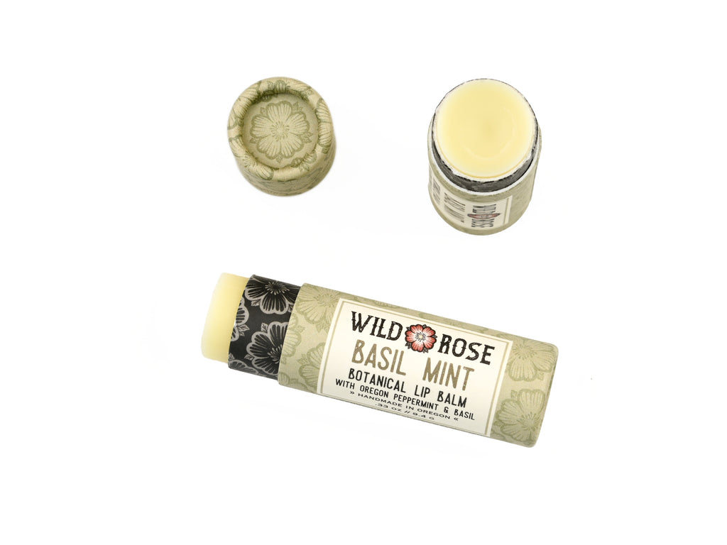Basil Mint Natural Lip Balm in a biodegradable paper tube on a white background. The cap is off revealing a creamy light green balm. 