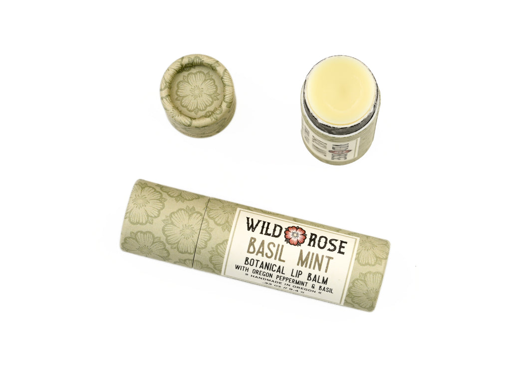 Basil Mint Natural Lip Balm in a biodegradable paper tube on a white background. The cap is off revealing a creamy light green balm. 