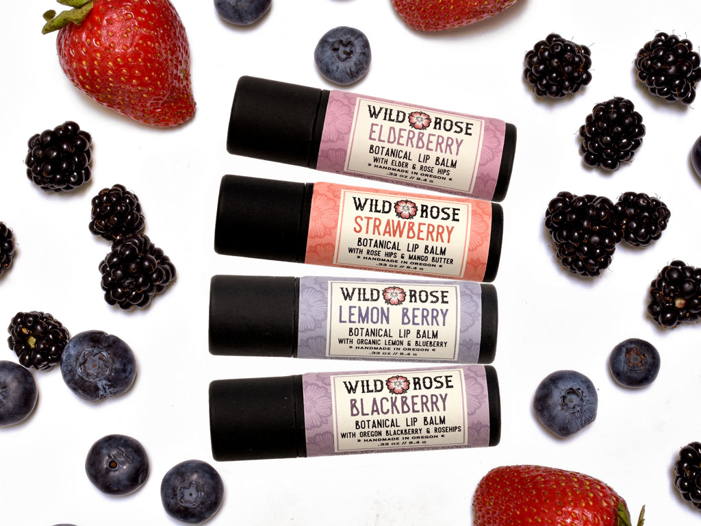Berry Lip Balm set including Elderberry, Strawberry, Lemon Berry and Blackberry in biodegradable paper tubes. Fresh berries surround.