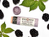 Blackberry Natural Lip Balm in a biodegradable paper tube. The cap is off revealing a creamy soft pink balm. Blackberries and leaves surround.