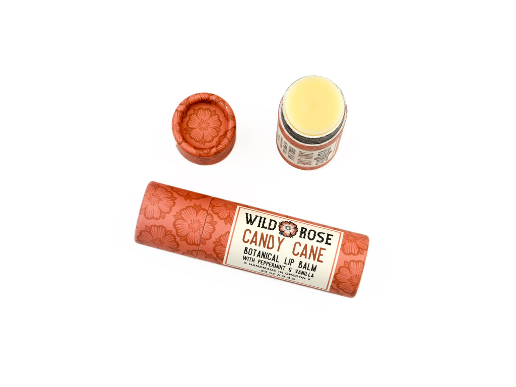 Candy Cane Natural Lip Balm in a biodegradable paper tube on a white background. The cap is removed, revealing a creamy white balm. 