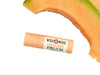 Wild Rose Cantaloupe Botanical Lip Balm in a peach-colored biodegradable paper tube with a white label, shown on a white background with a cantaloupe melon slice in the upper right corner.