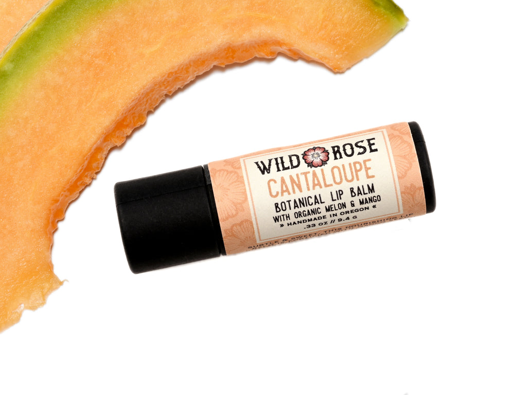 Cantaloupe Natural Lip Balm in a biodegradable paper tube. Fresh cantaloupe slices surround.