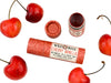 Wild Rose Cherry Vanilla Botanical Lip & Cheek Tint in a biodegradable tube, surrounded by fresh cherries on a white background.