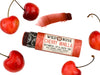 Wild Rose Cherry Vanilla Botanical Lip & Cheek Tint in a biodegradable tube on a white background with fresh cherries surrounding. The cap is removed revealing a dark red creamy tinted balm.