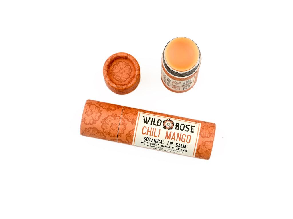 Wild Rose Chili Mango Botanical Lip Balm shown with its orange patterned tube, separate cap, and open balm container on a white background.