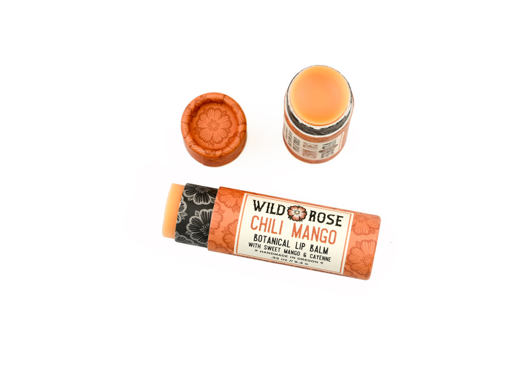 Wild Rose Chili Mango Botanical Lip Balm shown with its orange patterned tube, separate orange cap, and open balm stick on a white background.