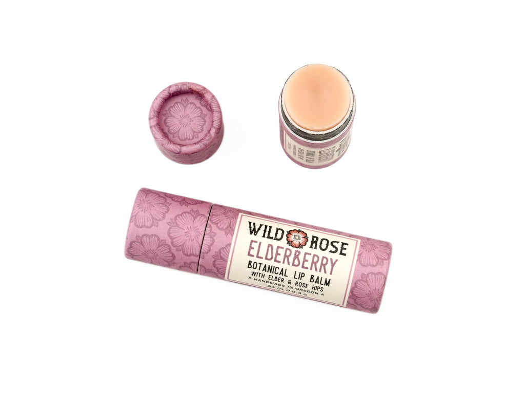 Elderberry Natural Lip Balm from Wild Rose  in a biodegradable paper tube on a white background. The cap is off revealing a creamy, light pink balm.