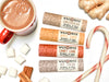 Wild Rose Holiday Lip Balm set with Gingerbread, Apple Cider, Candy Cane and Hot Cocoa Lip Balms in biodegradable tubes. Shown with candy canes, a cup of hot cocoa, marshmallows, ginger root and cinnamon on a white background.