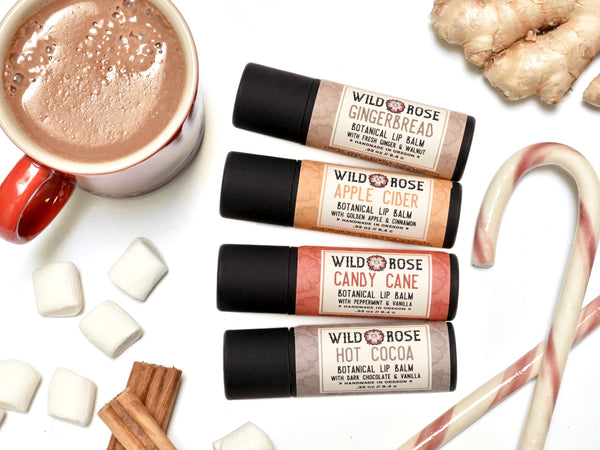 Holiday Natural Lip Balm Set with Candy Cane, Hot Cocoa, Apple Cider and Gingerbread. Packaged in large biodegradable paper tubes. Candy canes, hot cocoa, cinnamon and ginger surround.