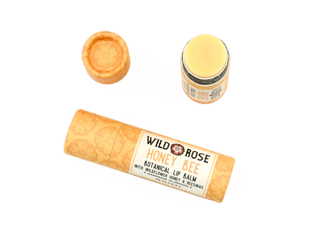 Honey Bee Natural Lip Balm from Wild Rose in a biodegradable paper tube on a white background. The cap is removed, revealing a creamy yellow balm.
