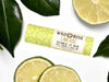 Wild Rose Limeade Botanical Lip Balm in a biodegradable tube on a white background with fresh lime slices and green leaves. 