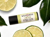 Limeade Lip Balm in a biodegradable paper tube. Fresh lime slices and leaves surround.