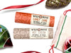 Wild Rose Holiday Lip Balm Stocking Stuffer Set with Candy Cane and Hot Cocoa Lip Balms on a white background. Ornaments and ribbon surround. Shown with a cotton gift bag with red and green stitching.