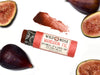 Wild Rose Mandarin Fig Botanical Lip & Cheek Tint in a biodegradable tube on a white background with fresh figs surrounding. The cap is removed revealing a dark red creamy tinted balm.