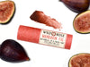 Wild Rose Mandarin Fig Botanical Lip & Cheek Tint in a biodegradable tube on a white background with fresh figs surrounding. A color swatch of the tint is above.
