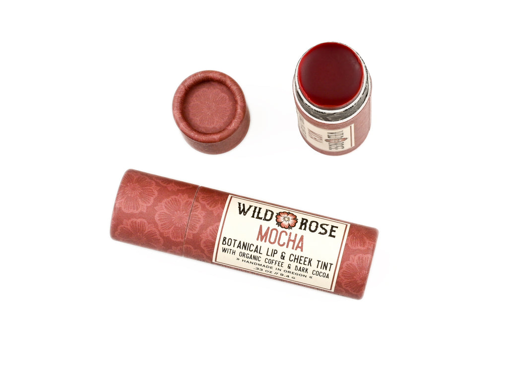 Wild Rose Mocha Botanical Lip & Cheek Tint in a biodegradable paper tube on a white background. The cap is removed, revealing a dark red tint.