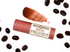 Wild Rose Mocha Botanical Lip & Cheek Tint in a biodegradable paper tube on a white background with coffee beans surrounding. A color swatch is above, revealing a dark red tint.