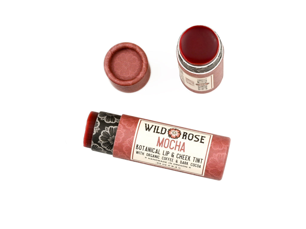 Wild Rose Mocha Botanical Lip & Cheek Tint in a biodegradable paper tube on a white background. The cap is removed, revealing a dark red tint.