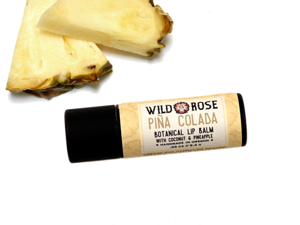 Piña Colada Natural Lip Balm in a biodegradable paper tube. Fresh pineapple slices surround.