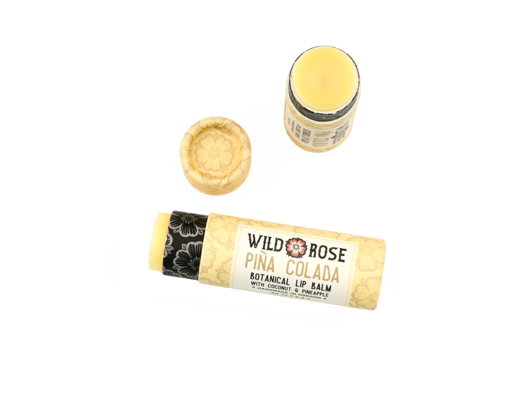 Wild Rose Piña Colada Botanical Lip Balm in a biodegradable tube on a white background. The cap is off, revealing a creamy yellow balm.