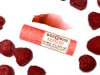 Wild Rose Raspberry Botanical Lip & Cheek Tint in a biodegradable paper tube on a white background with fresh raspberries. A color swatch is above, revealing a dark red tint.