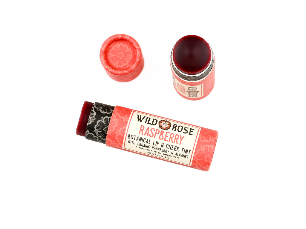 Wild Rose Raspberry Botanical Lip & Cheek Tint in a biodegradable paper tube on a white background. The cap is removed, revealing a dark red tint.
