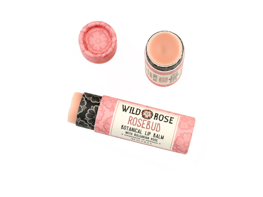 Wild Rose Rosebud Botanical Lip Balm in a biodegradable tube on a white background. The cap is removed revealing a creamy pink balm.