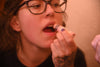 A close-up lifestyle shot of a person with glasses applying Wild Rose Botanical lip balm from a pink biodegradable tube to their lips.