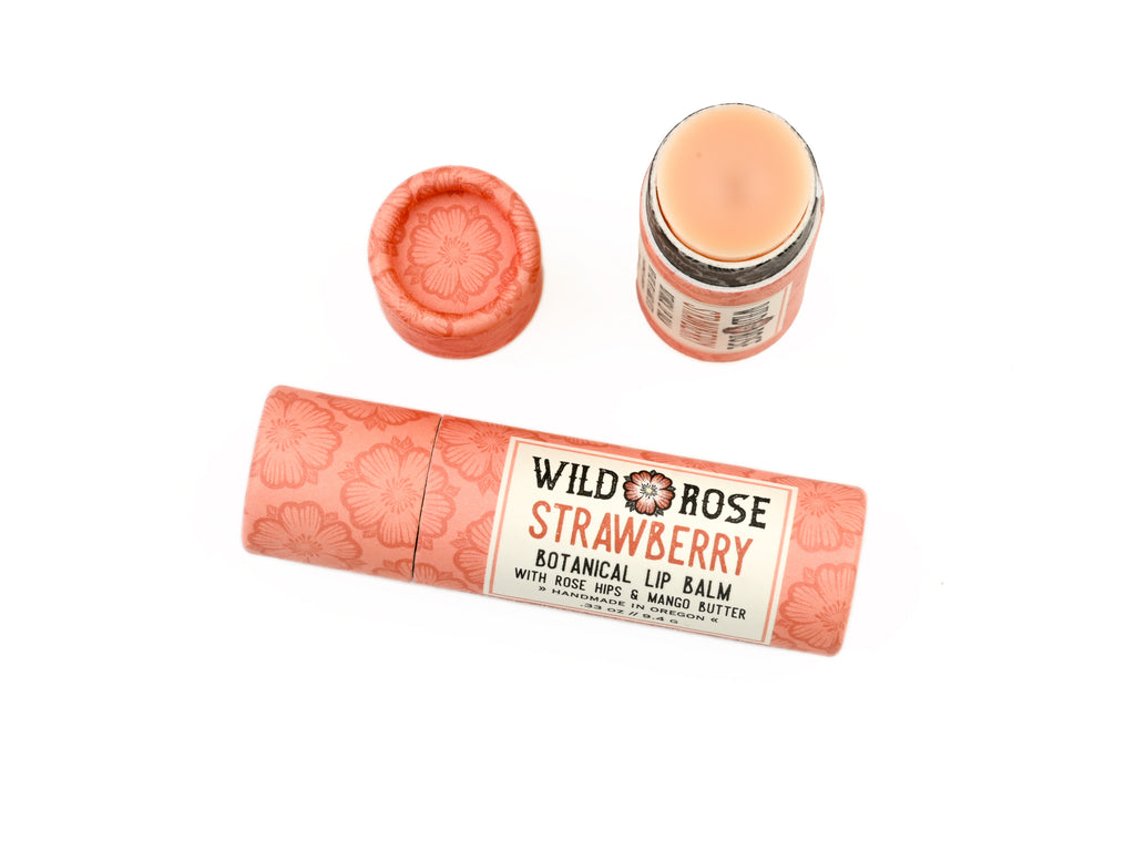 Wild Rose Strawberry Botanical Lip Balm in a biodegradable tube on a white background.. The cap is removed revealing a creamy pink balm.