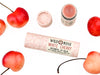 Wild Rose White Cherry Botanical balm in a biodegradable tube, surrounded by fresh cherries.
