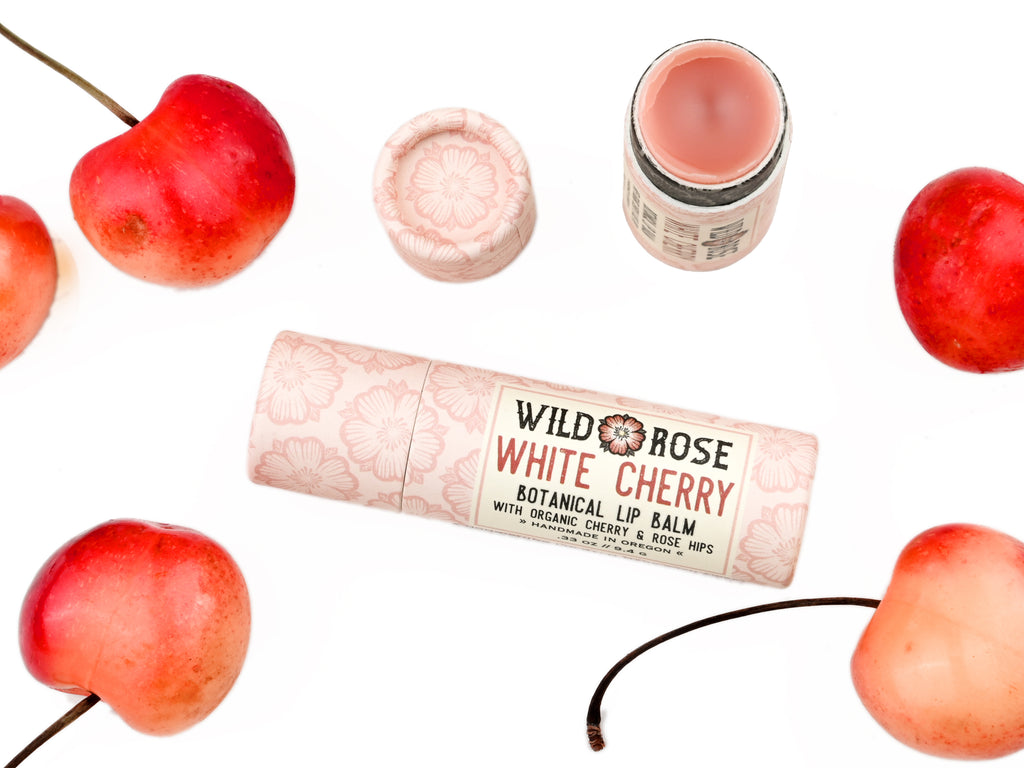 Wild Rose White Cherry Botanical balm in a biodegradable tube, surrounded by fresh cherries.