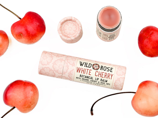 Wild Rose White Cherry Botanical balm in a biodegradable tube, surrounded by fresh cherries.
