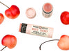 Wild Rose White Cherry Botanical balm in a biodegradable tube shown with the cap removed revealing a creamy pink balm. Surrounded by fresh cherries.