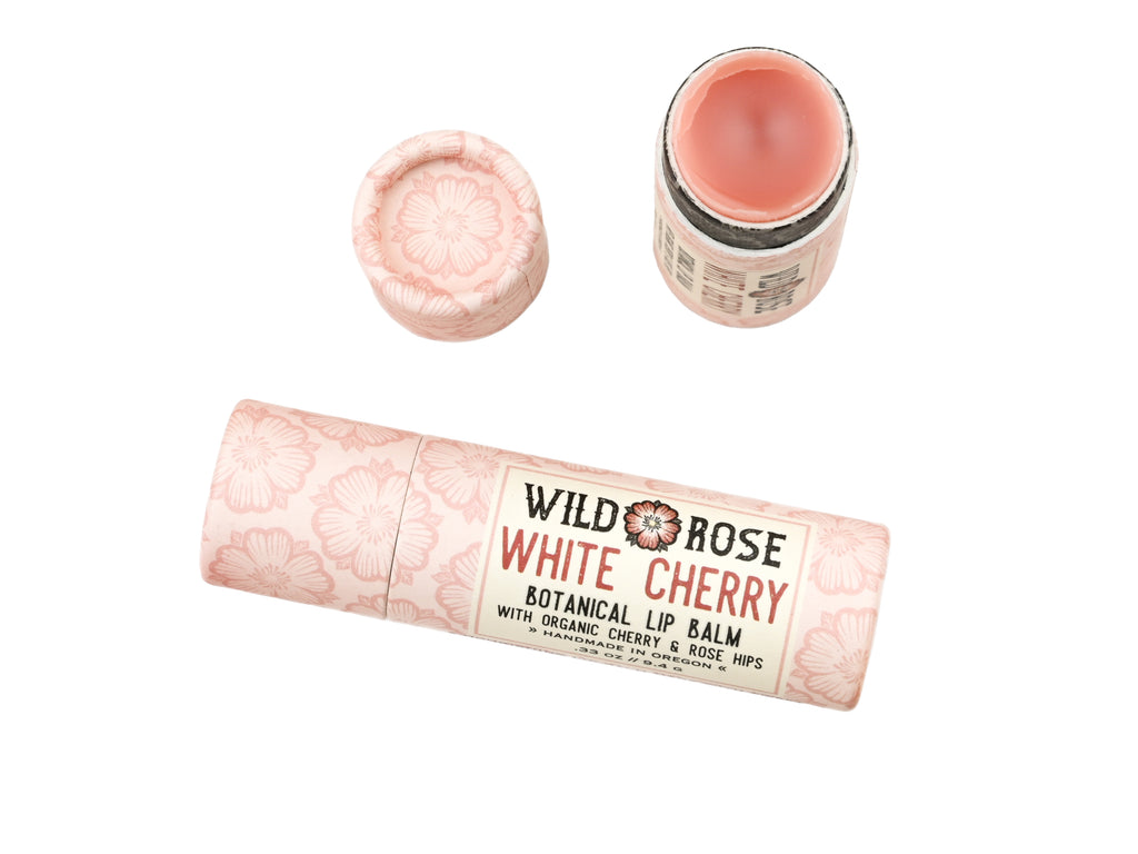Wild Rose White Cherry Botanical balm in a biodegradable tube shown with the cap removed revealing a creamy pink balm on a white background.