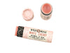 Wild Rose White Cherry Botanical balm in a biodegradable tube shown with the cap removed revealing a creamy pink balm. Surrounded by fresh cherries.